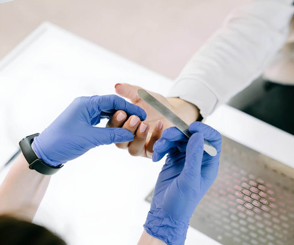 A nail technician wearing gloves carefully shaping and treating a client’s nails
